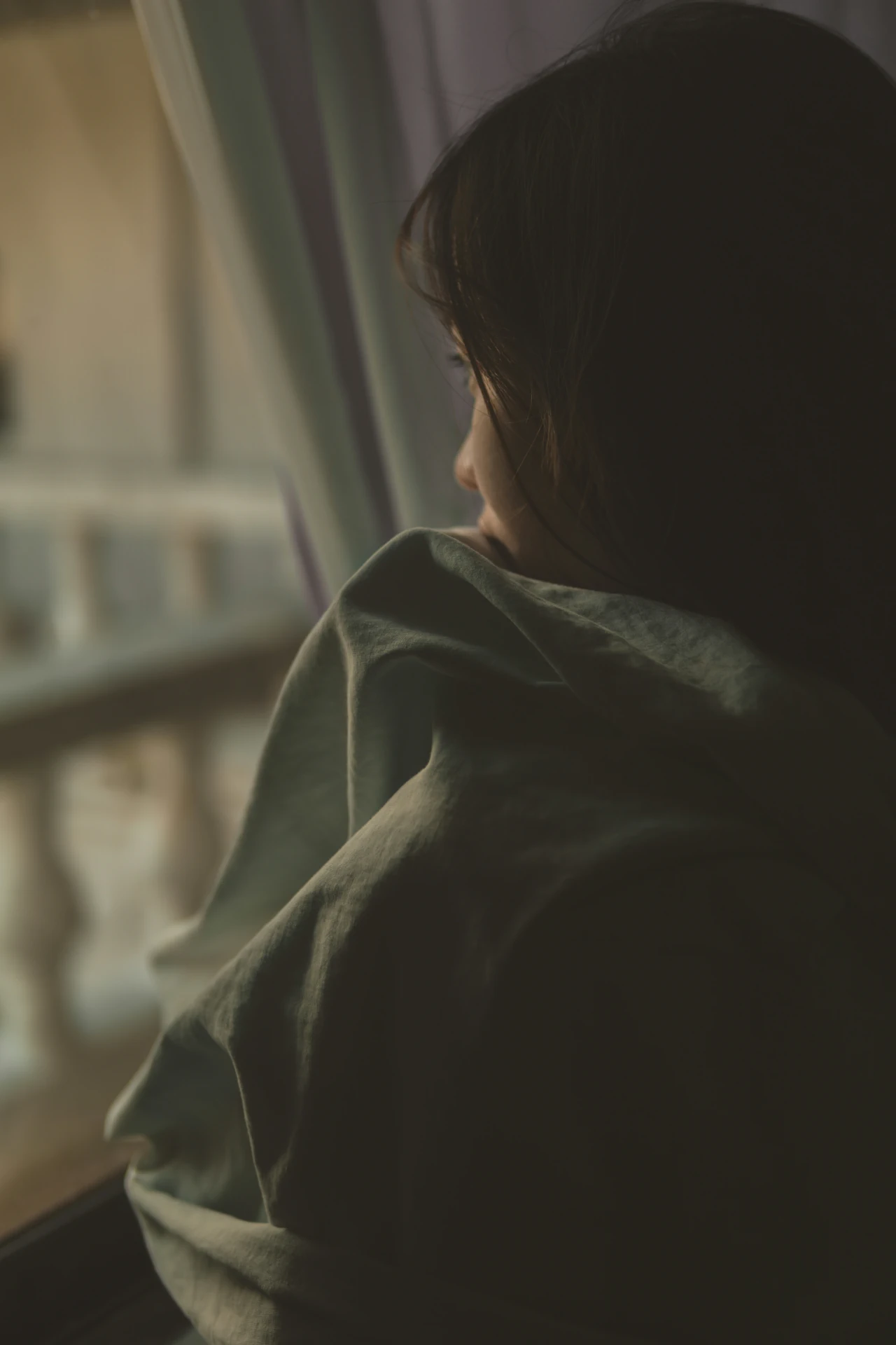 A woman wrapped in a sheet looking out of a window 
