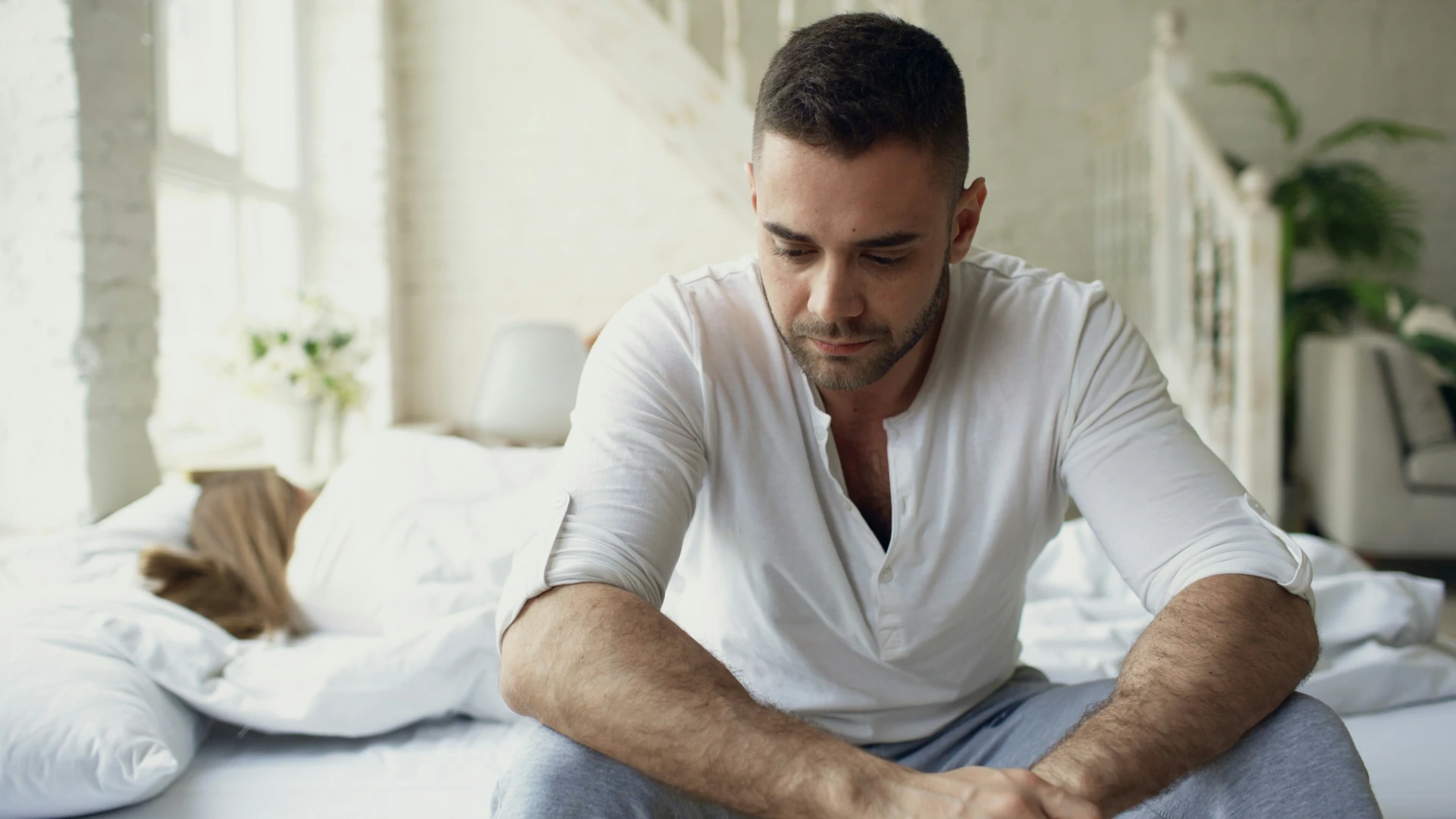 A man sitting on the edge of the bed with a woman laying in it